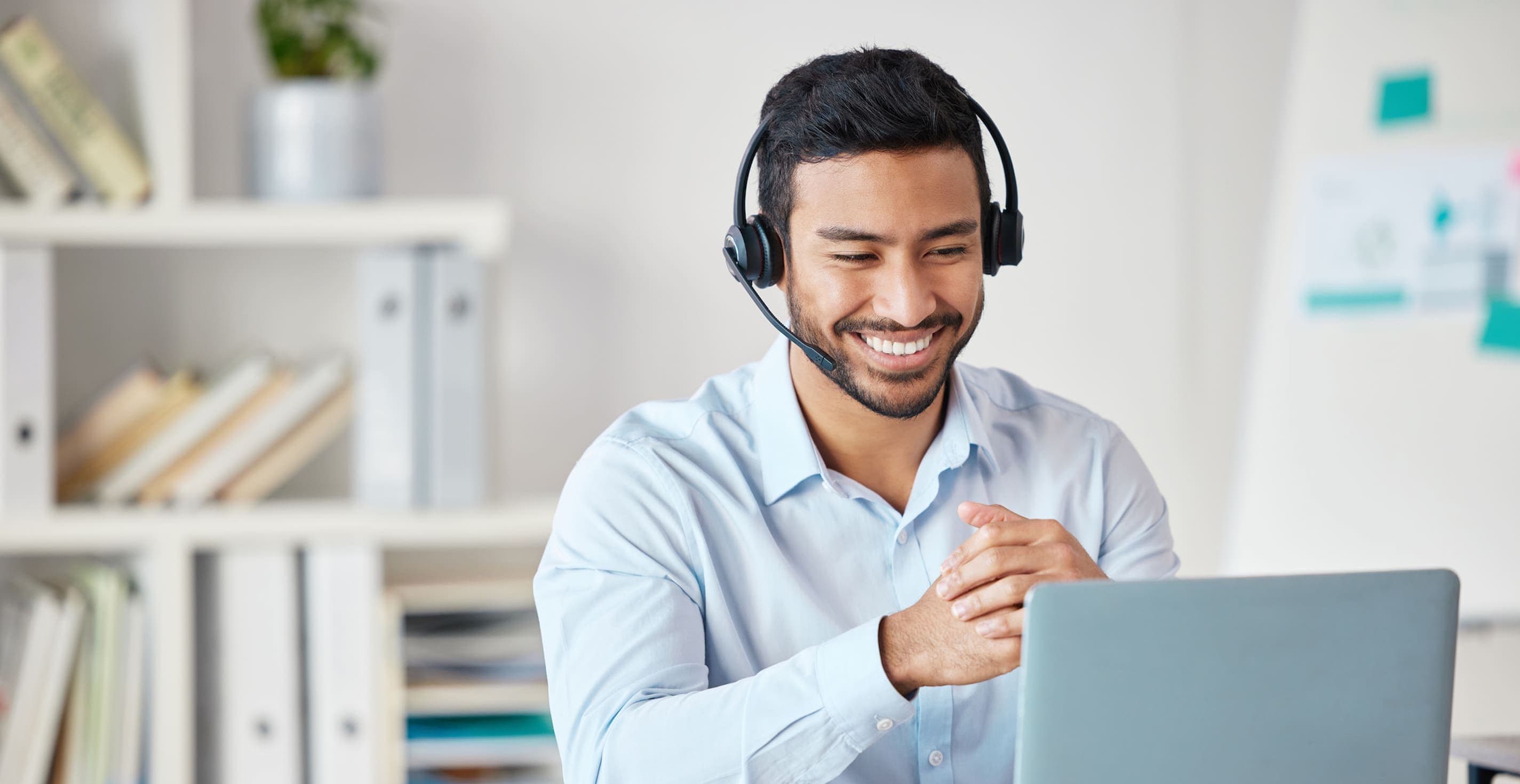 Closeup of smiling mixed race call center agent smiling while wearing headset. Young male customer service representative using wireless headset and consulting clients online while using a laptop.